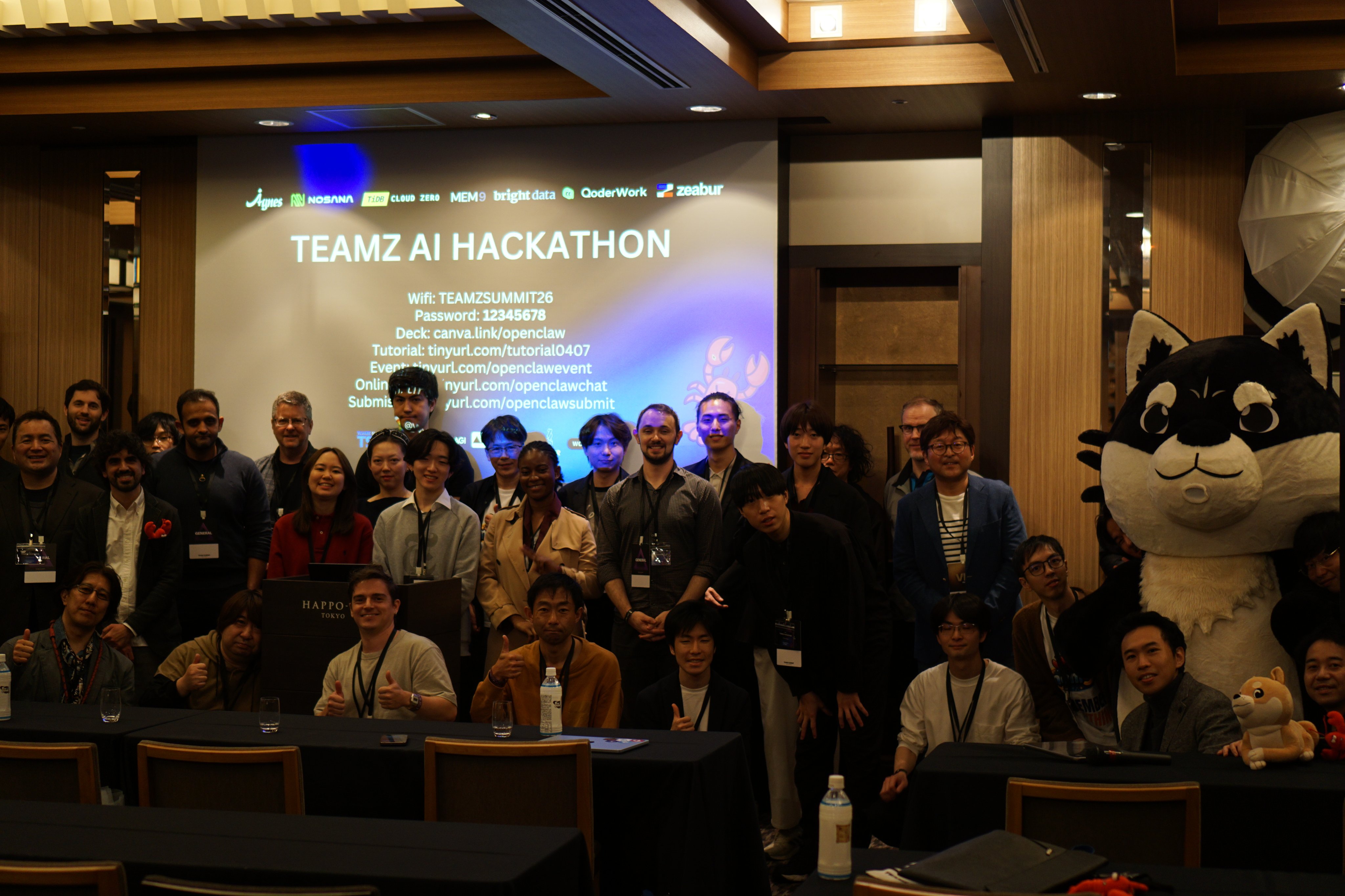TEAMZ AI Hackathon group photo with event banner and mascot in Tokyo